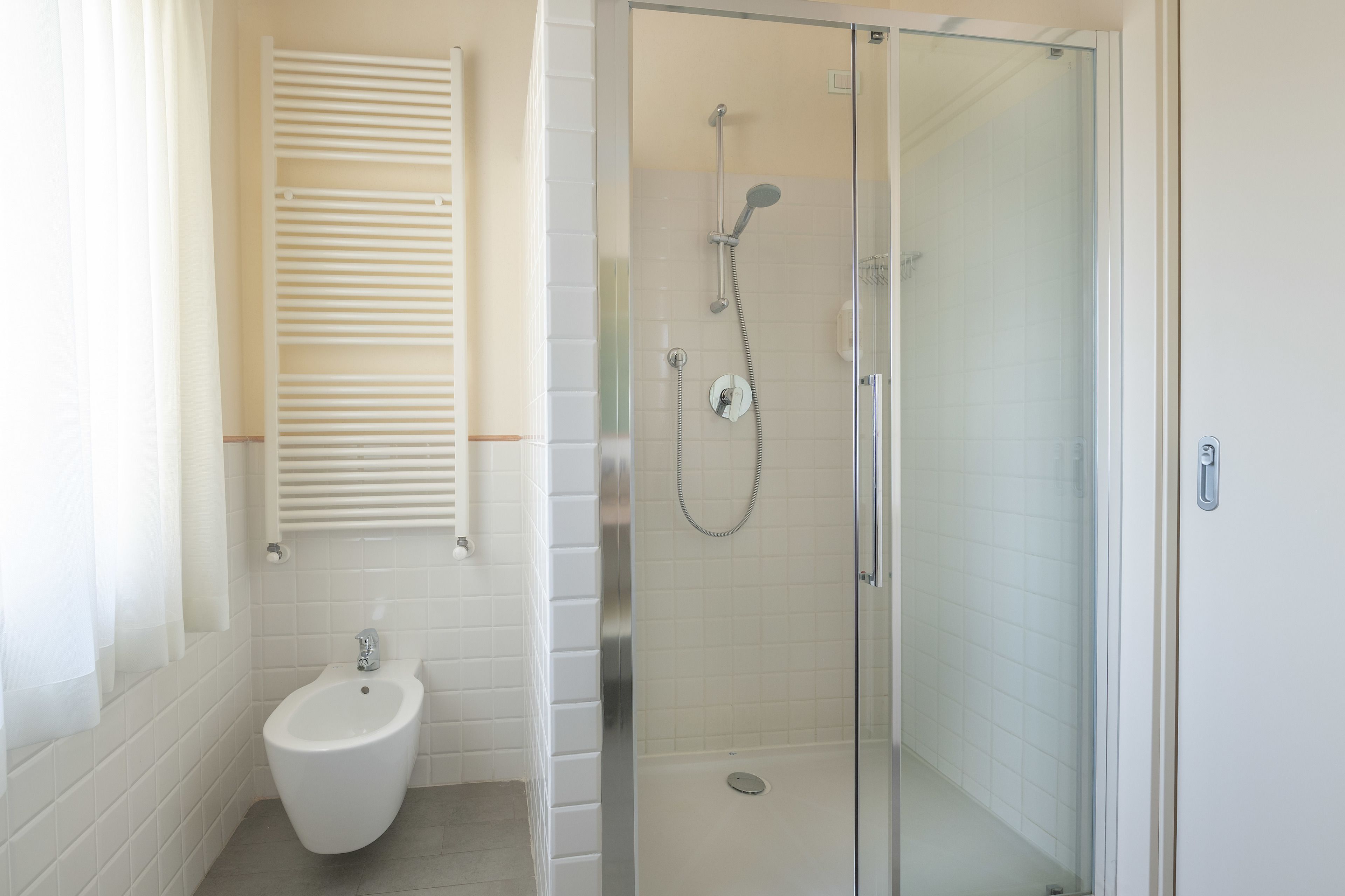 A modern bathroom with a glass-enclosed shower, a bidet, and a white tiled wall.