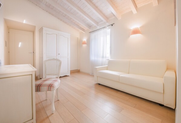 Una habitación amplia con un sofá blanco, una silla blanca, un armario blanco y suelo de madera.