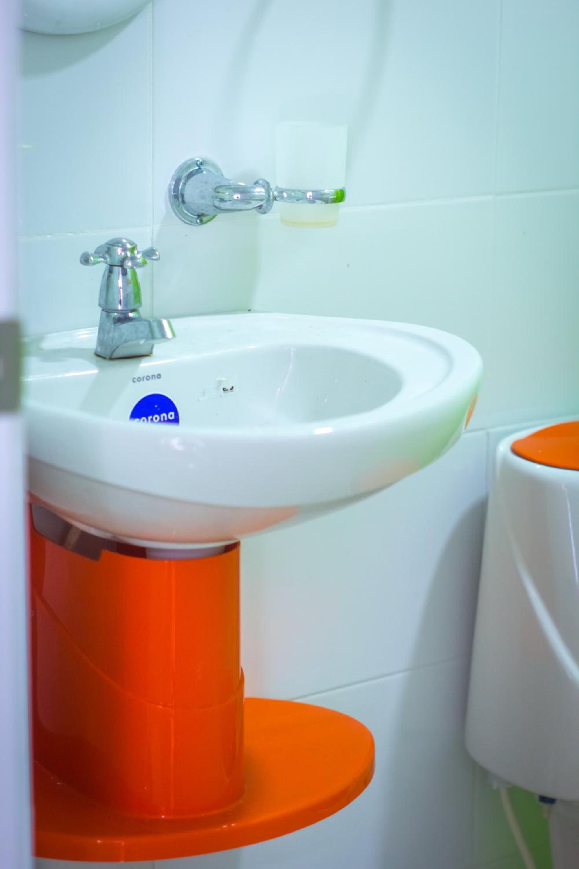 Un bagno con un lavandino bianco, un piedistallo arancione e un water bianco.