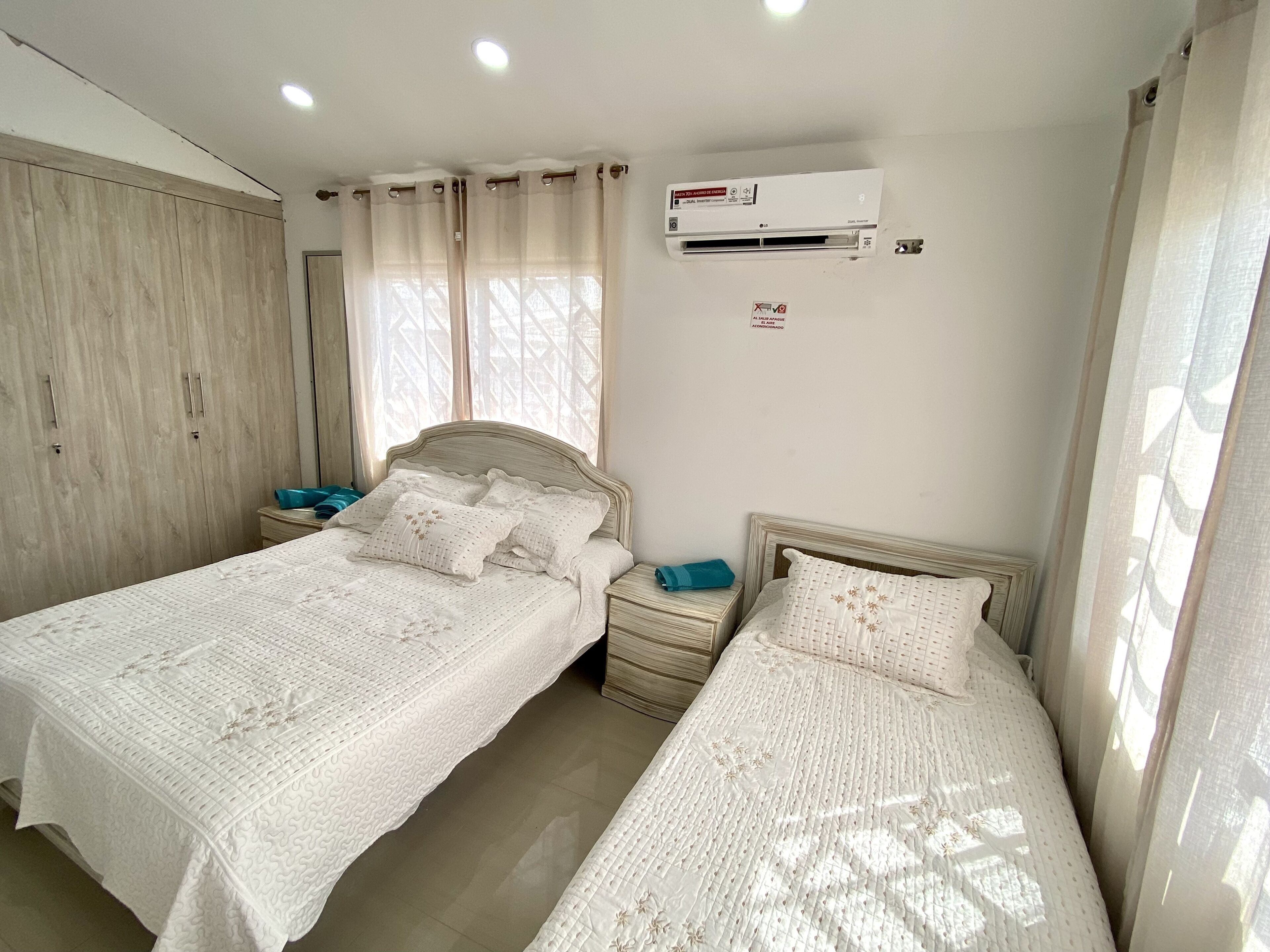 Een slaapkamer met twee bedden, een kledingkast, een airconditioning en een raam met gordijnen.