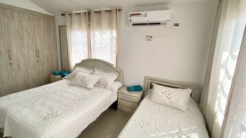 Een slaapkamer met twee bedden, een kledingkast, een airconditioning en een raam met gordijnen.