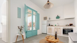 A modern kitchen with white cabinets, a teal door, and a dining area with a round table and chairs. - Ploes Seaside Houses (Naxos)