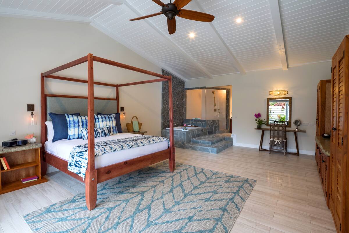 A spacious bedroom with a four-poster bed, a ceiling fan, and a bathroom with a stone shower area.