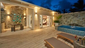 Un patio in legno con piscina, pareti in pietra e un interno accogliente visibile attraverso una porta aperta.