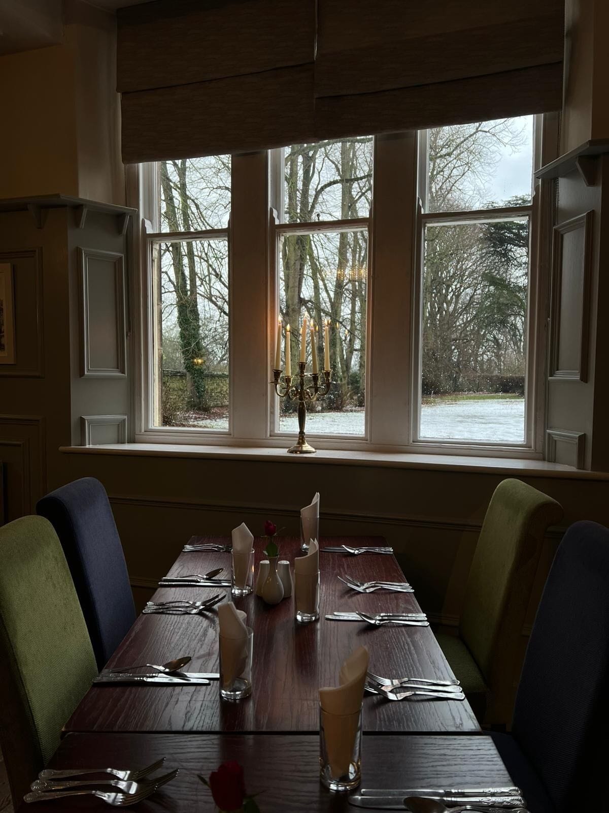 Een eettafel voor twee, met uitzicht op bomen door grote ramen.