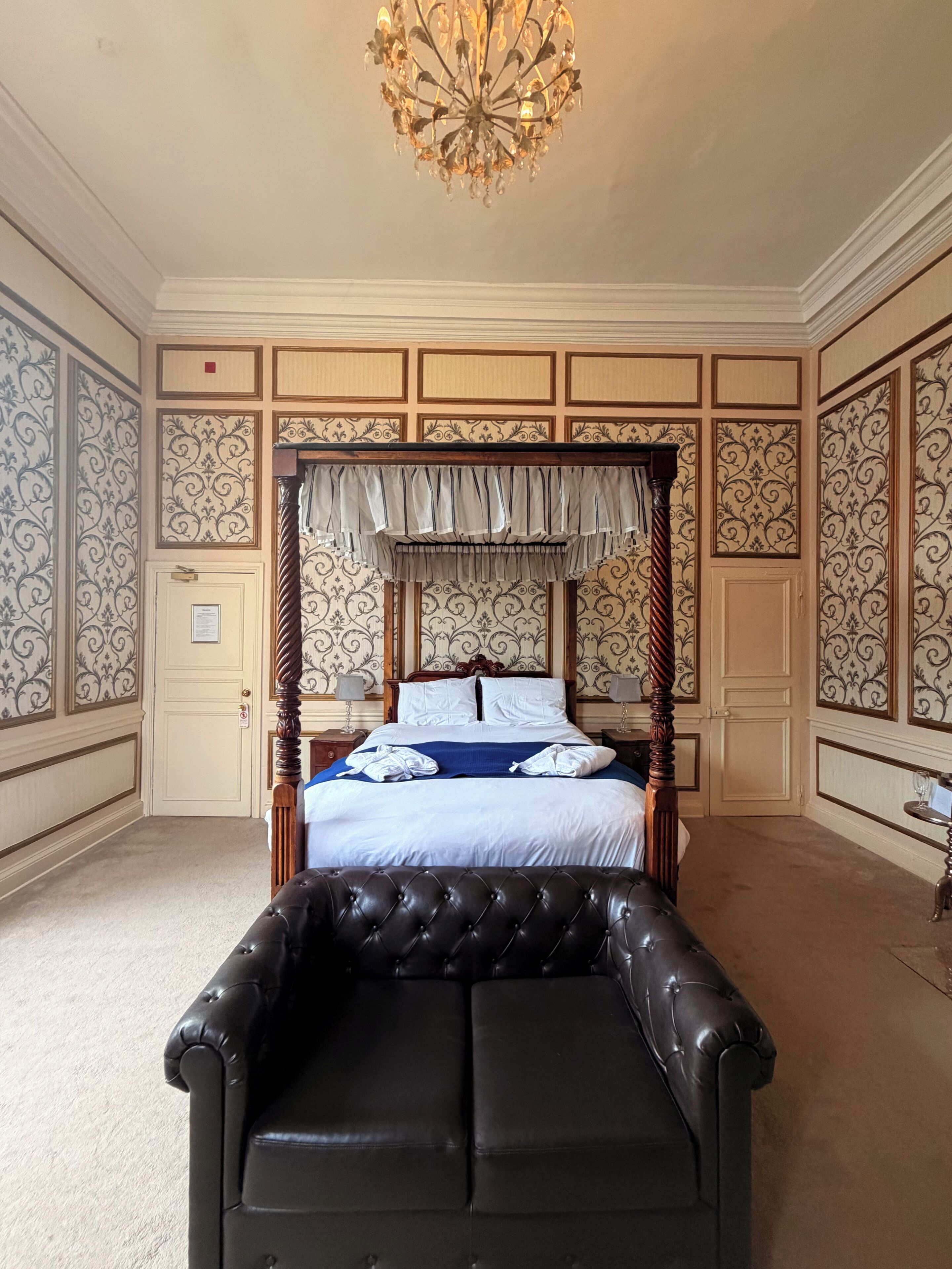 A four-poster bed with a canopy, a tufted leather sofa, and a chandelier.