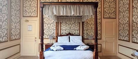 A four-poster bed with a canopy, a tufted leather sofa, and a chandelier.