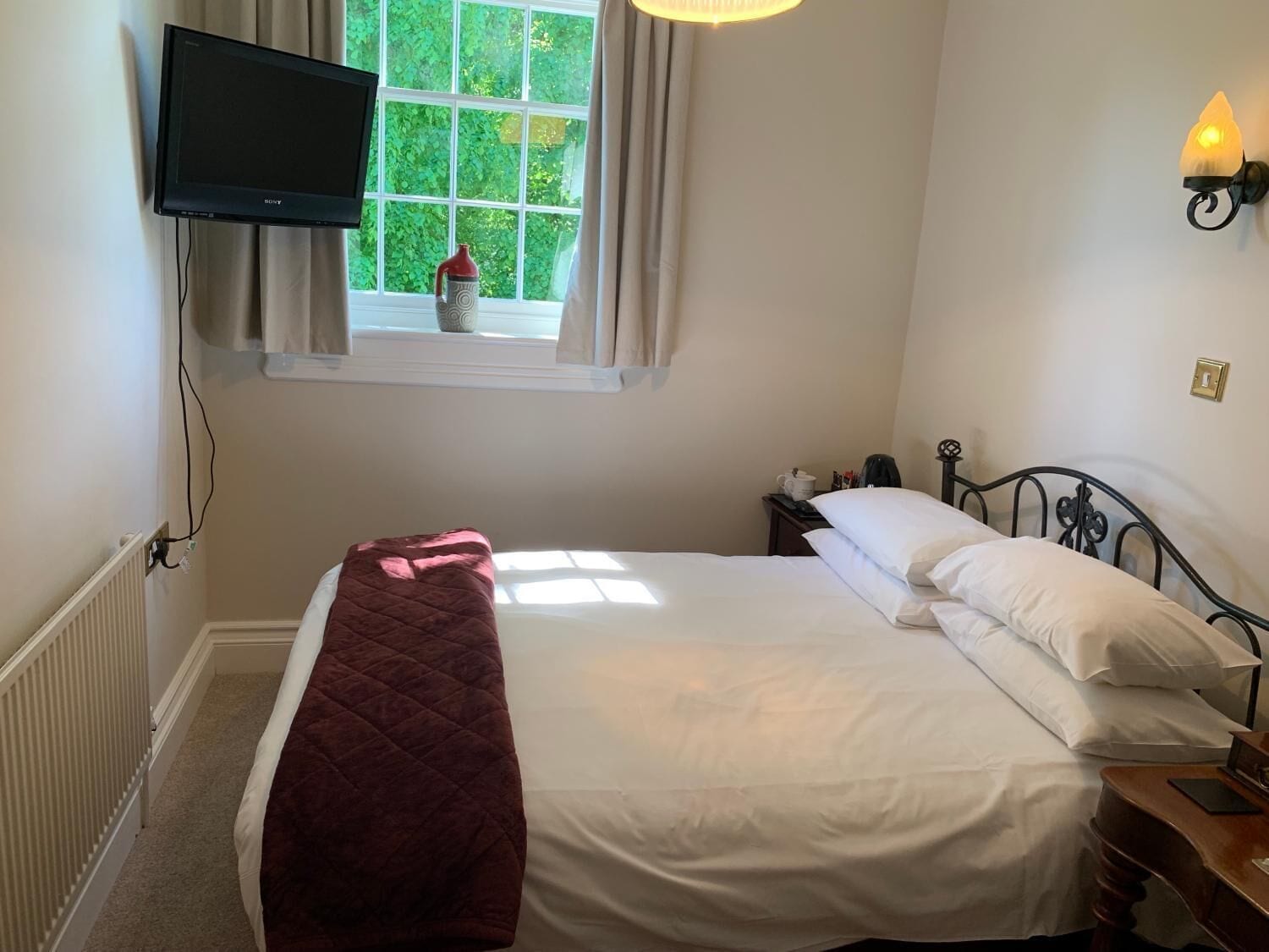 A bedroom with a bed, a bedside table, a lamp, a window with curtains, and a television mounted on the wall.