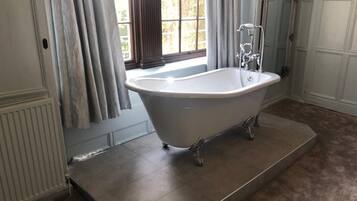A freestanding bathtub in a bathroom with a large window, a radiator, and a door with paneling.