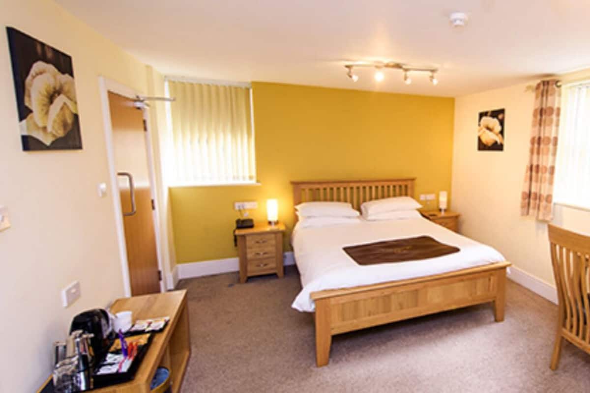 A bedroom with a bed, bedside tables, a desk with a chair, a mirror, and a window with curtains.