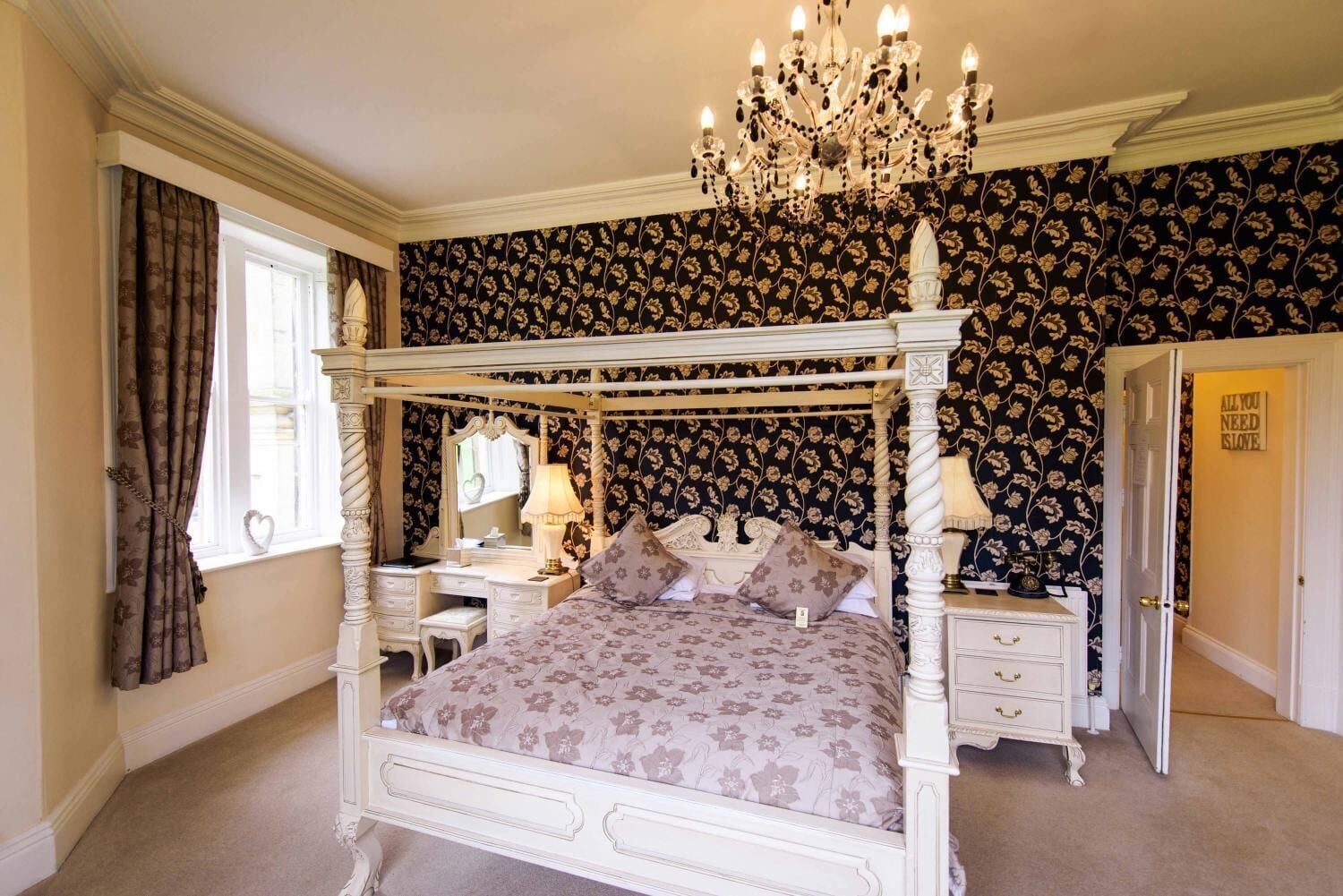 A four-poster bed with a chandelier, a vanity with a mirror, and a door with a sign.