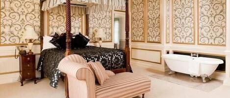 Un lit à baldaquin, une chaise longue, une baignoire blanche et une table de chevet avec une lampe.