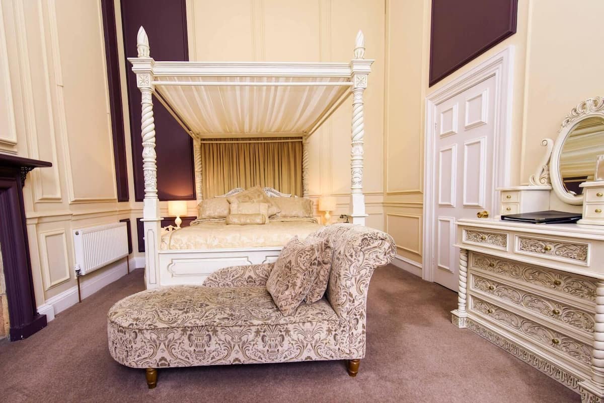 A four-poster canopy bed with a matching four-poster chair, a dresser with a mirror, and a radiator.