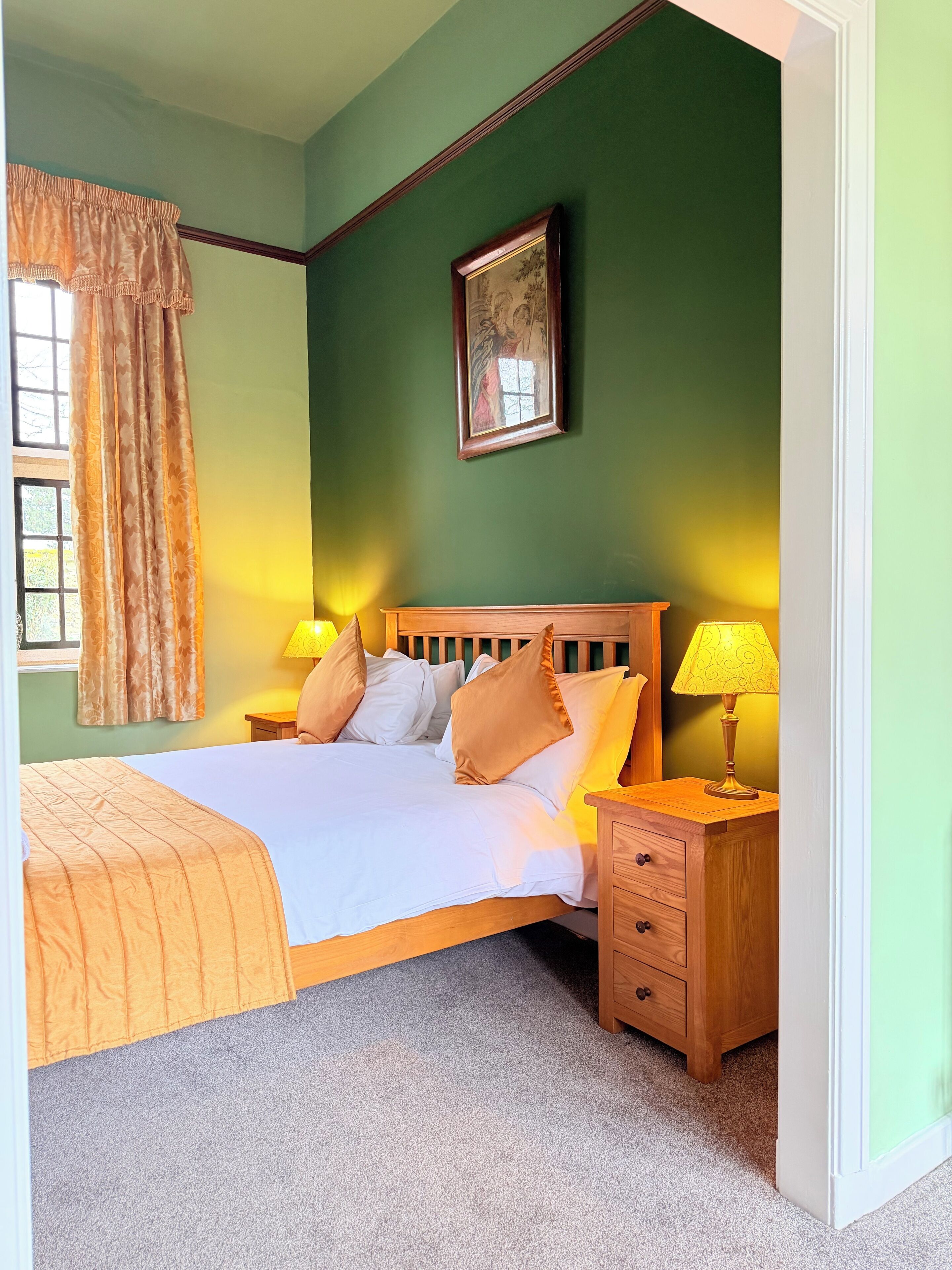A neatly made bed with a wooden headboard, two bedside tables with lamps, a window with curtains, and a framed picture on the wall.