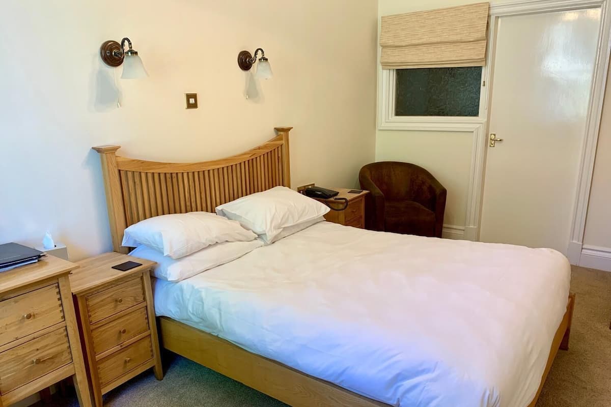 A neatly made bed with white linens, a wooden headboard, and two wall-mounted lamps.