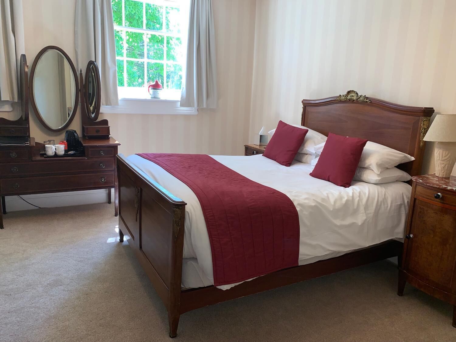 A bedroom with a wooden bed, two nightstands, a dresser, and a window with curtains.