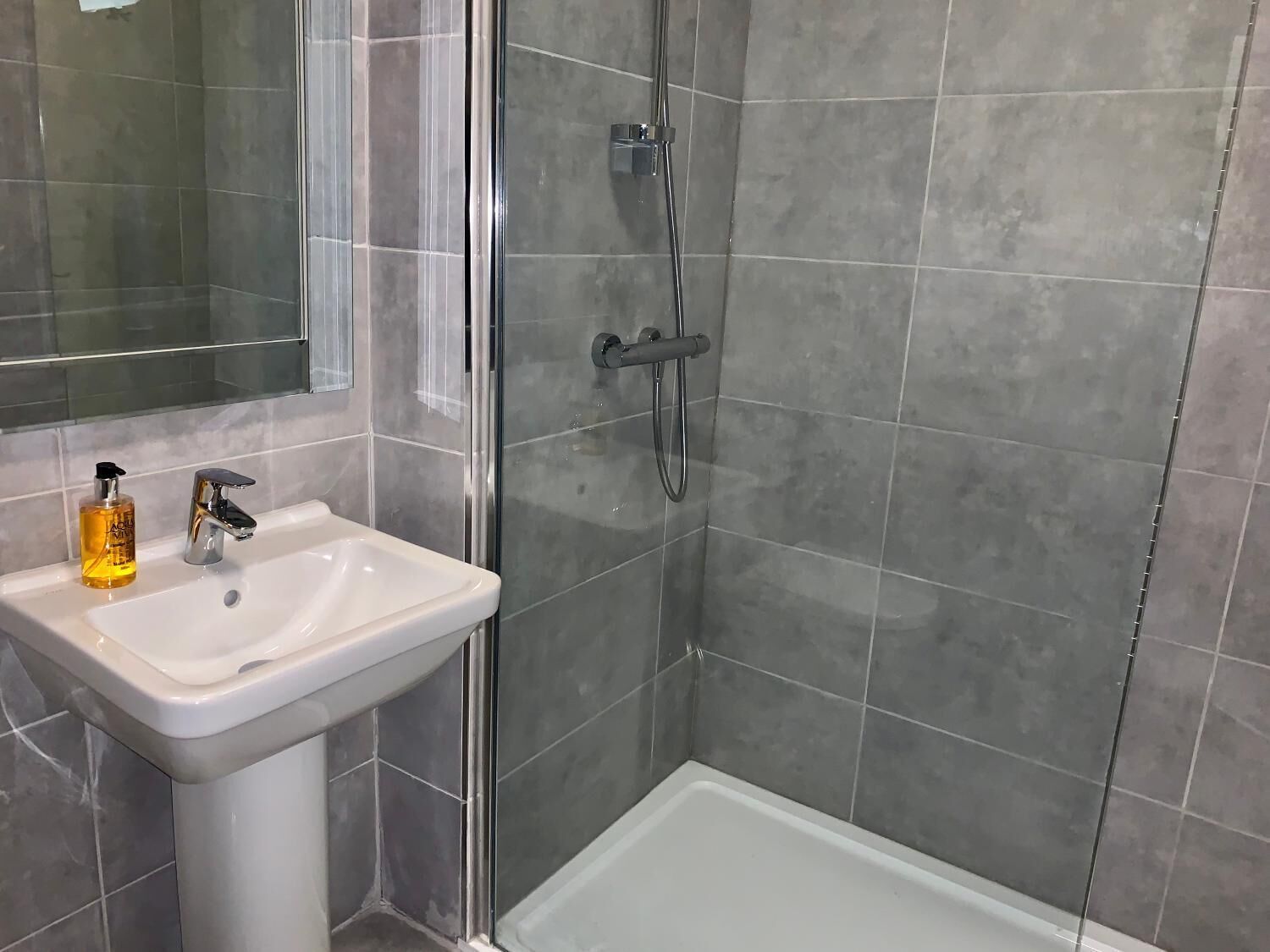 Une salle de bain avec un lavabo blanc, un miroir et un espace douche aux carreaux gris.