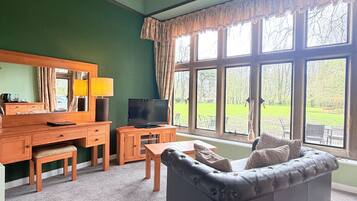 A living room with a dark leather sofa, wooden furniture, a television, and large windows with curtains.