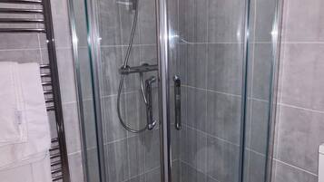 A glass-enclosed shower with a handheld showerhead and a handheld faucet.