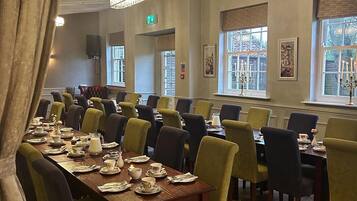 A dining area with multiple tables and chairs, a chandelier, and windows with views.