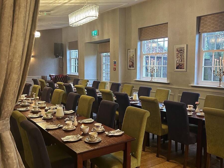 A dining area with multiple tables and chairs, a chandelier, and windows with views.