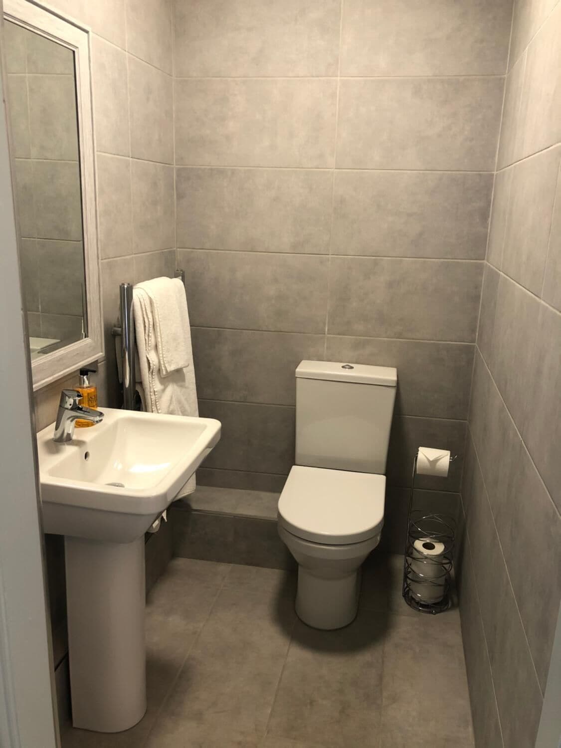 Un baño pequeño y moderno con lavamanos, inodoro y espejo blancos.
