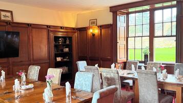 A dining area with wooden tables and chairs, a television, and a bookshelf.