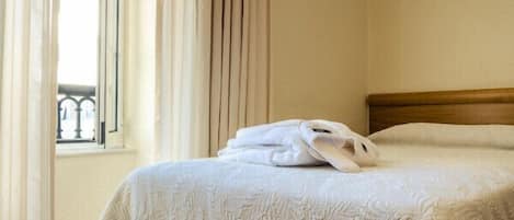 Una habitación de hotel con una cama bien hecha, una ventana con cortinas y un balcón con barandilla.