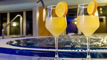 Dos cócteles con rodajas de naranja sobre una superficie reflectante cerca de una piscina.