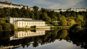 A large, historic building with a symmetrical facade, situated by a calm lake reflecting the structure. - Hotel Balneario de Lugo (Lugo)
