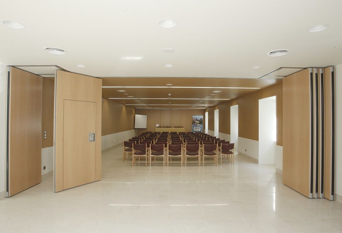 Un salón de conferencias con filas de sillas, una mesa y una pantalla al frente.