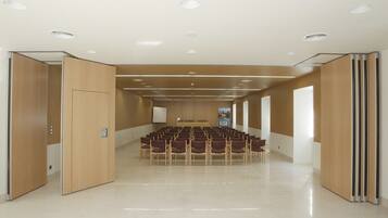 Un salón de conferencias con filas de sillas, una mesa y una pantalla al frente.