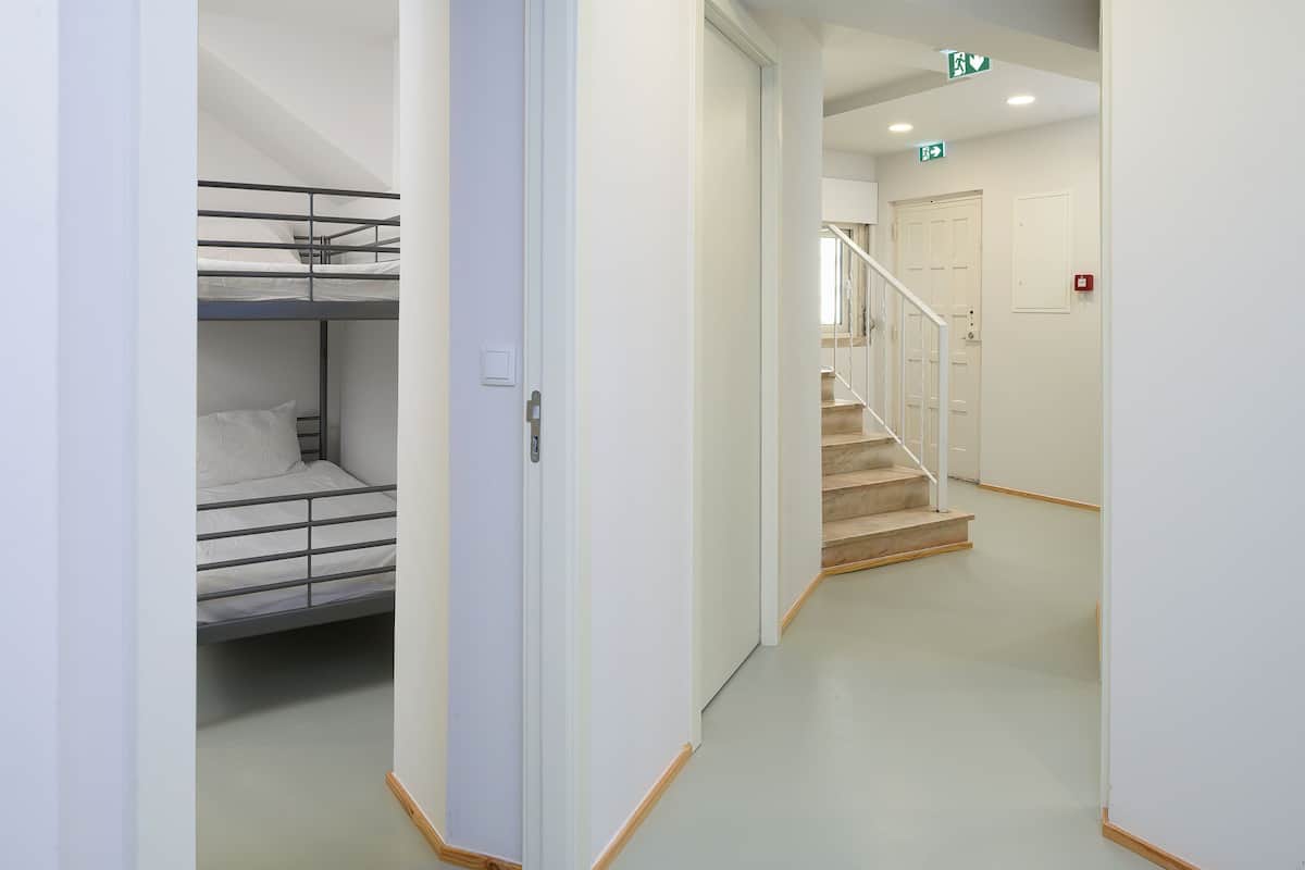 Habitación de hotel con literas, una puerta que da a una escalera y una señal de salida de emergencia visible.