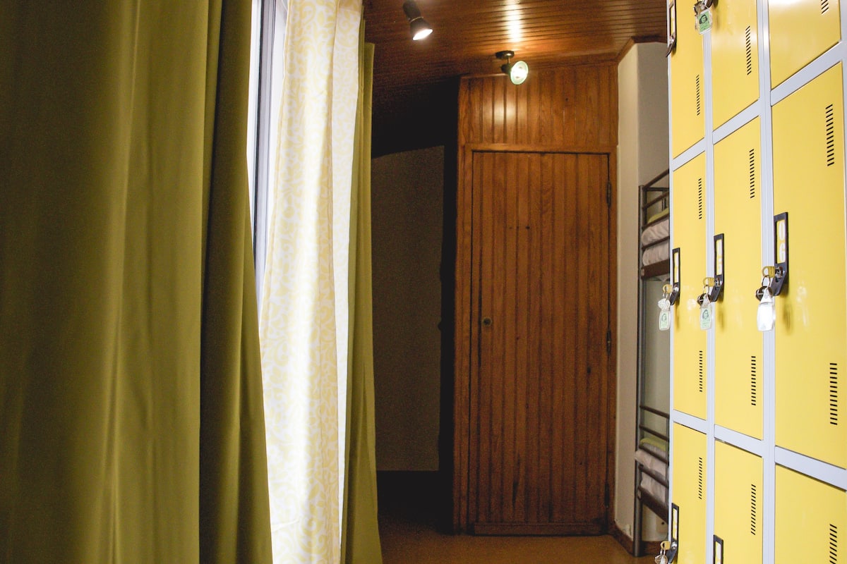 Un pasillo con techo de madera, cortinas verdes y taquillas amarillas.