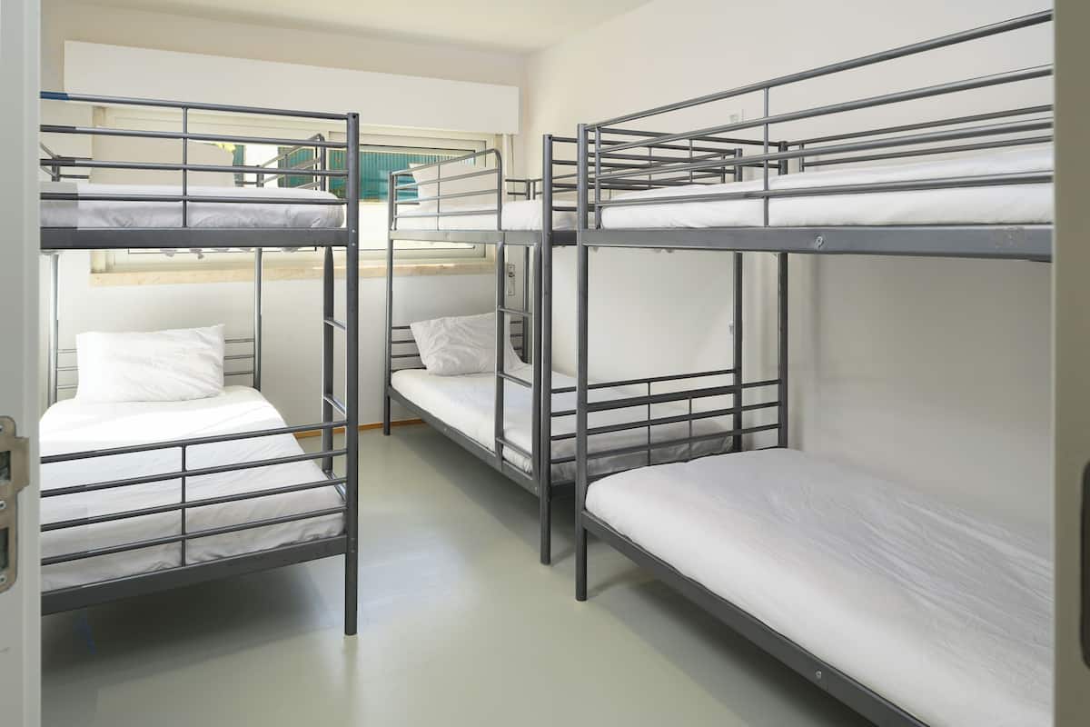 Un dormitorio con literas dispuestas en fila, cada una con colchón y almohada blancos.
