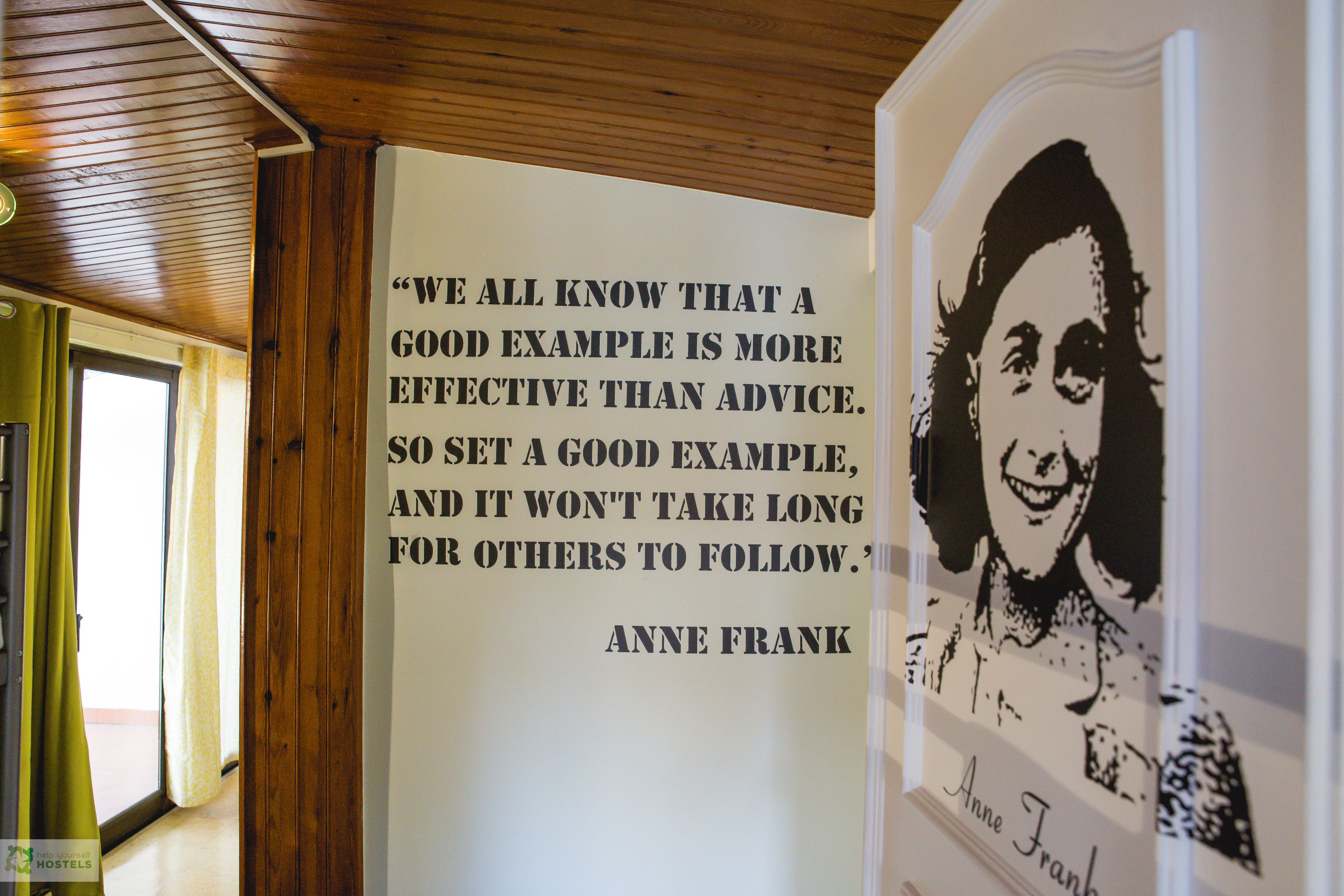 Una cita de Anne Frank en una pared dentro de una habitación con paneles de madera y una ventana.