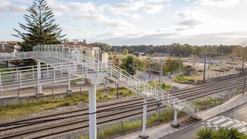 Una estación de tren con varias vías, un puente peatonal y un gran árbol de hoja perenne.