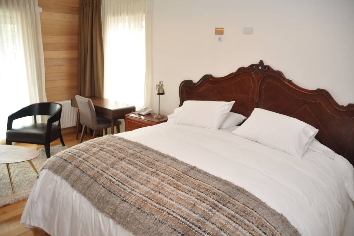 A neatly arranged bedroom with a large bed, a desk with a chair, and a lamp.