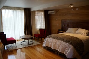 Ett hotellrum med en sänggavel i trä, en säng med vita sängkläder, en röd stol, ett litet runt bord och en vit matta.