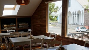A dining area with wooden tables and chairs, a skylight, and a view of the street outside. - Hotel Boutique Refugio de Navegantes (Dalcahue)