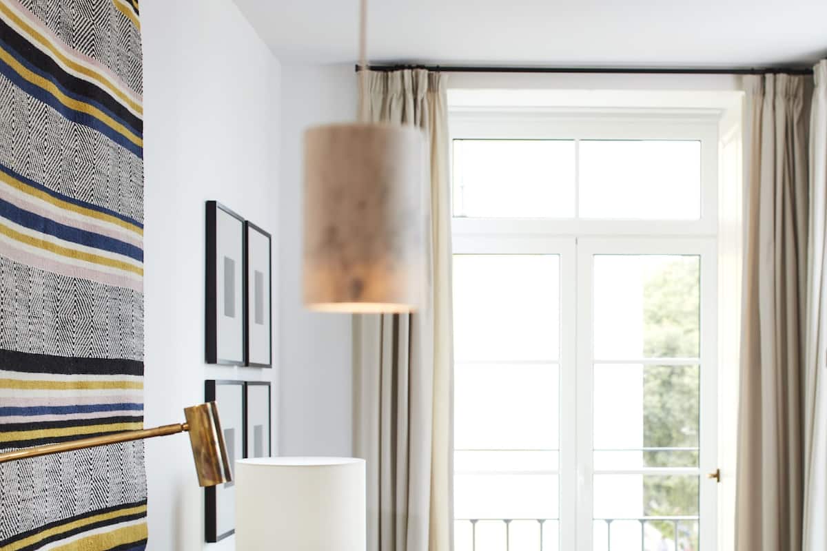 Una camera d'albergo moderna con un divano grigio scuro, un tavolino con una lampada, una poltrona e vista sull'esterno attraverso un'ampia finestra.