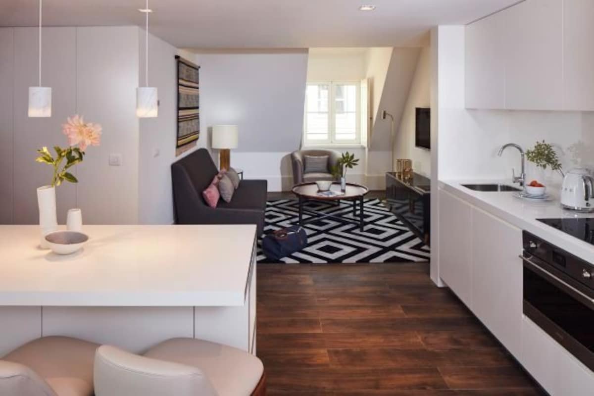 A modern kitchen with a central island, a dining area with a black and white patterned rug, and a living area with a sofa and a coffee table.