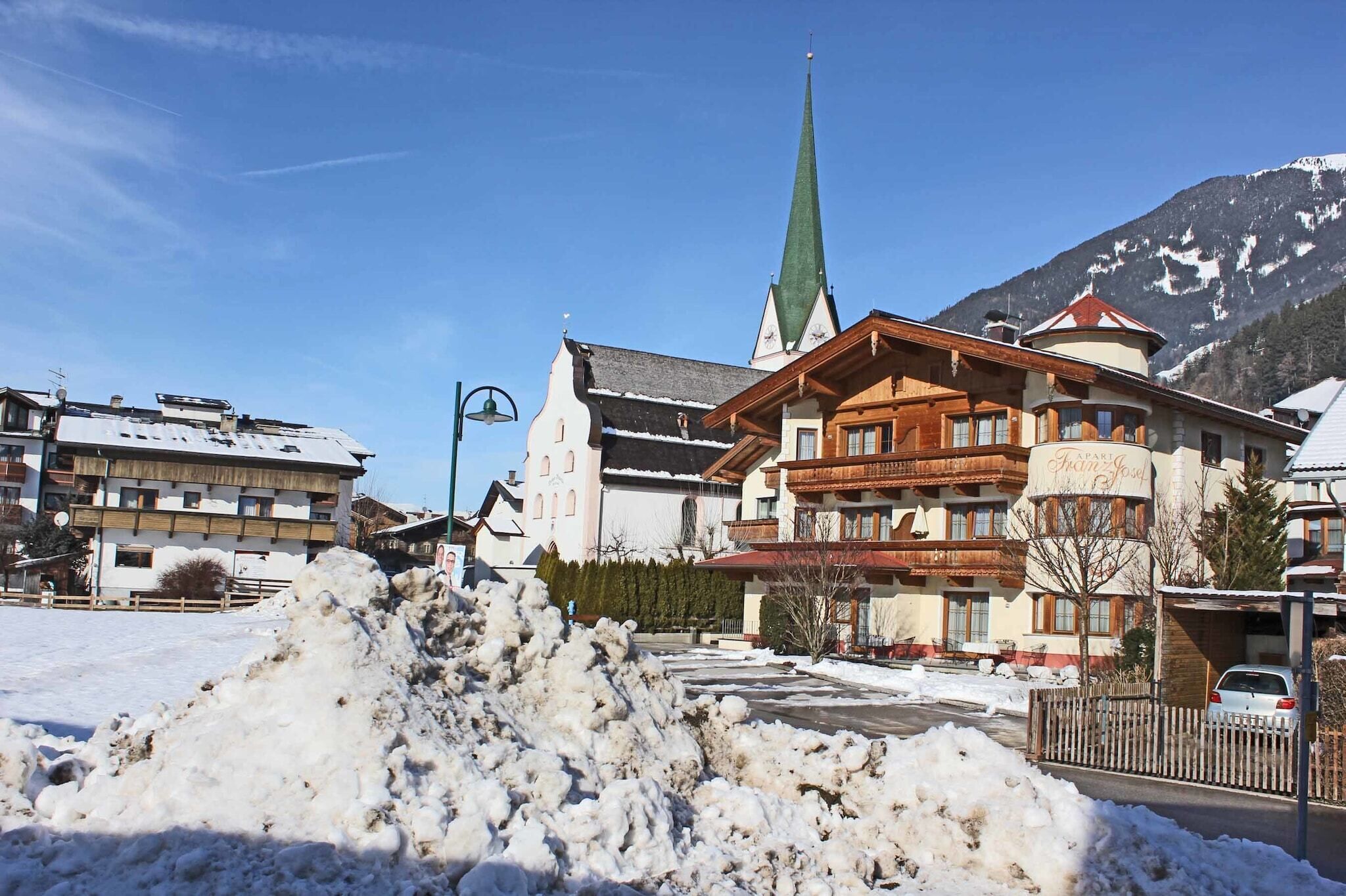A hotel with a traditional Alpine architectural style, featuring a prominent church steeple and a snow-covered landscape.
