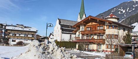 A hotel with a traditional Alpine architectural style, featuring a prominent church steeple and a snow-covered landscape.
