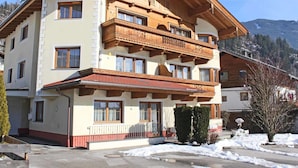 A multi-story building with wooden balconies, a sloped roof, and a mountainous backdrop.