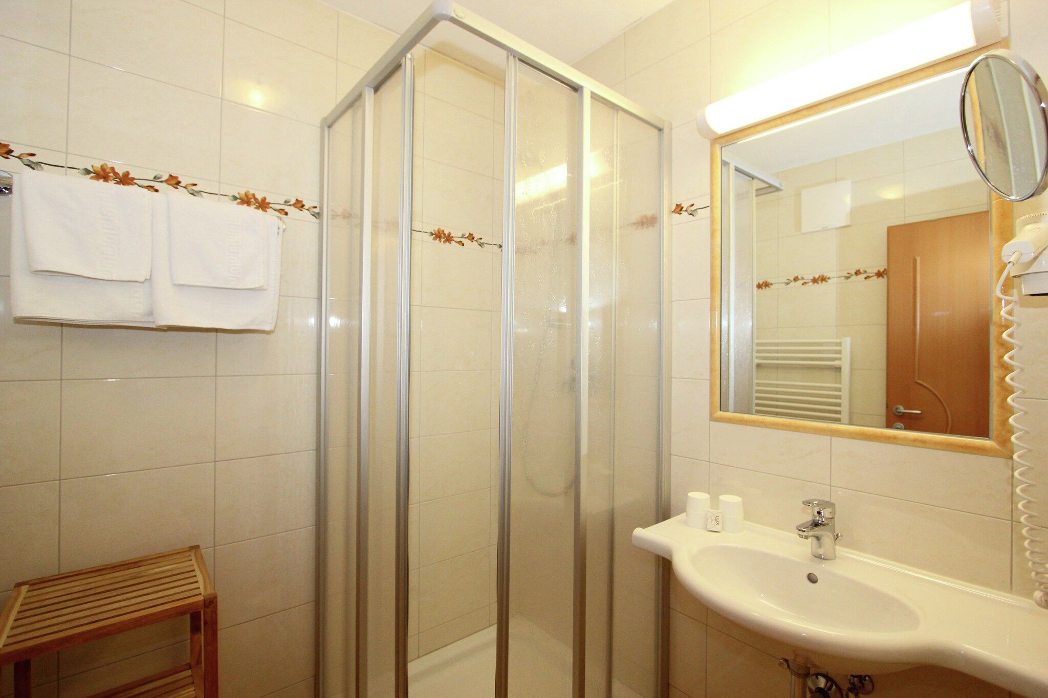 A bathroom with a glass shower enclosure, a sink with a mirror, and two towels hanging on the wall.