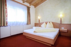 A hotel room with a bed, two bedside lamps, a window with curtains, and a radiator.