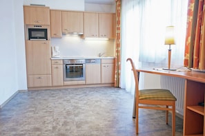 A compact kitchen with a built-in oven, a coffee maker, and a dining area with a chair.