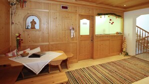A wooden interior with a table, benches, and a small statue.