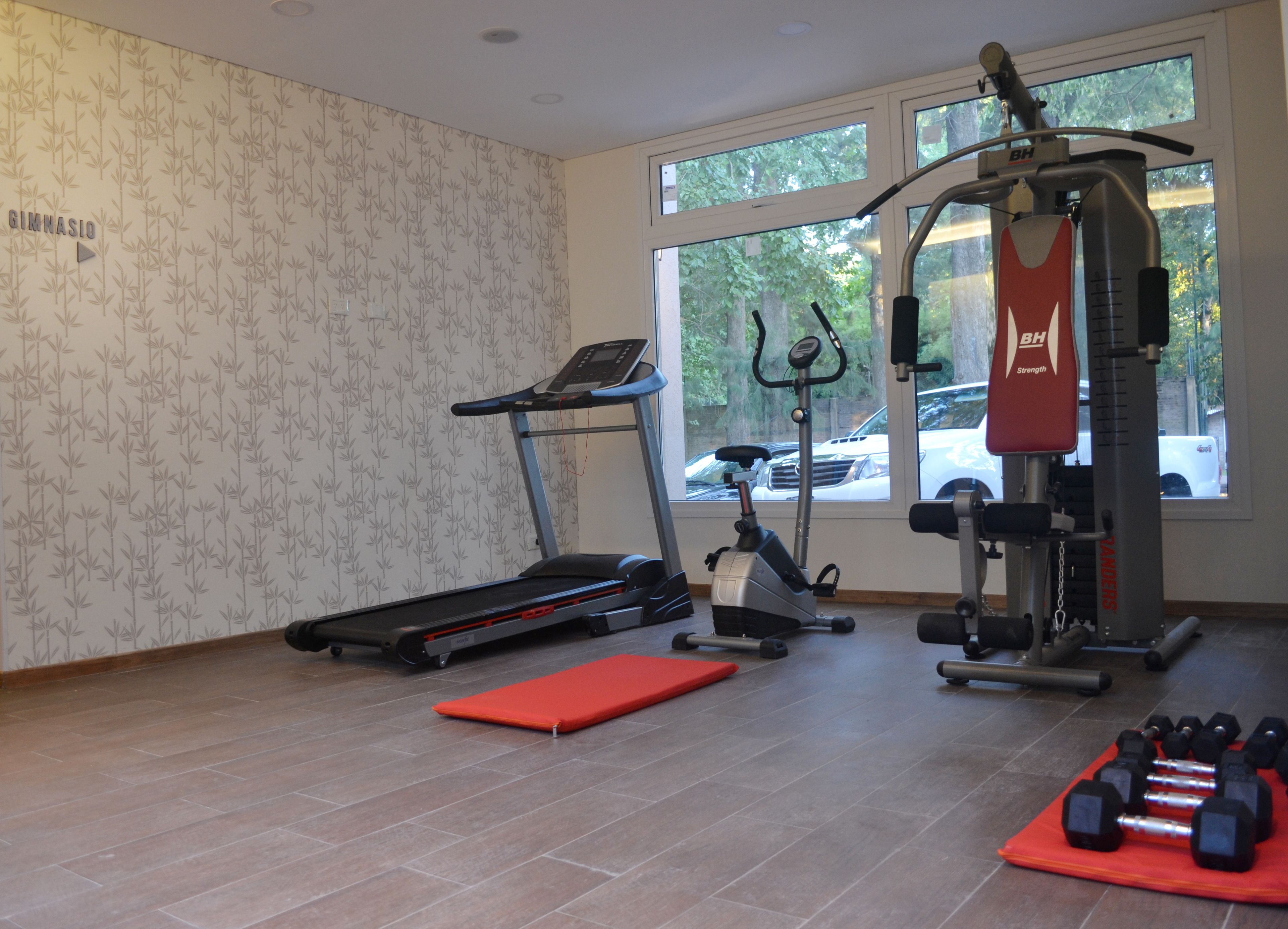Un gimnasio con cinta de correr, elíptica, máquina de pesas y mancuernas.